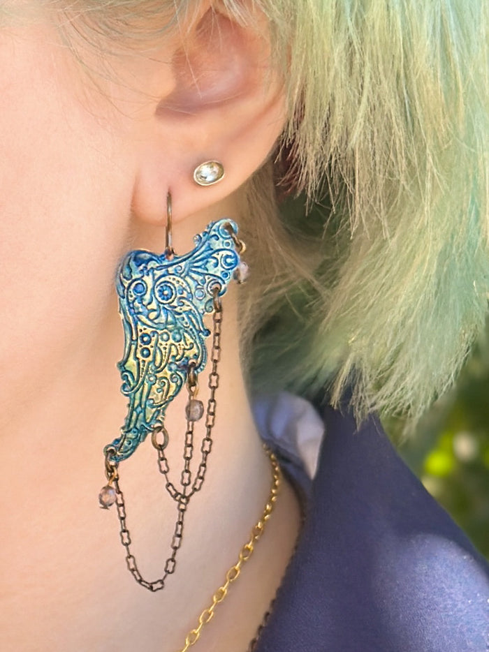 Ear with blue wing earring and chains.