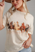 A woman wearing a cream-colored short-sleeve t-shirt with a graphic print of running horses, paired with light blue jeans and a brown hat.